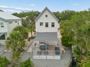 Une maison à deux étages dotée d’un patio couvert, entourée d’arbres et baignée par un ciel dégagé.