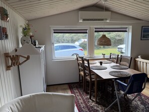 Un coin repas avec une table dressée pour quatre personnes, un réfrigérateur blanc et une fenêtre donnant sur une voiture et de la verdure à l’extérieur.