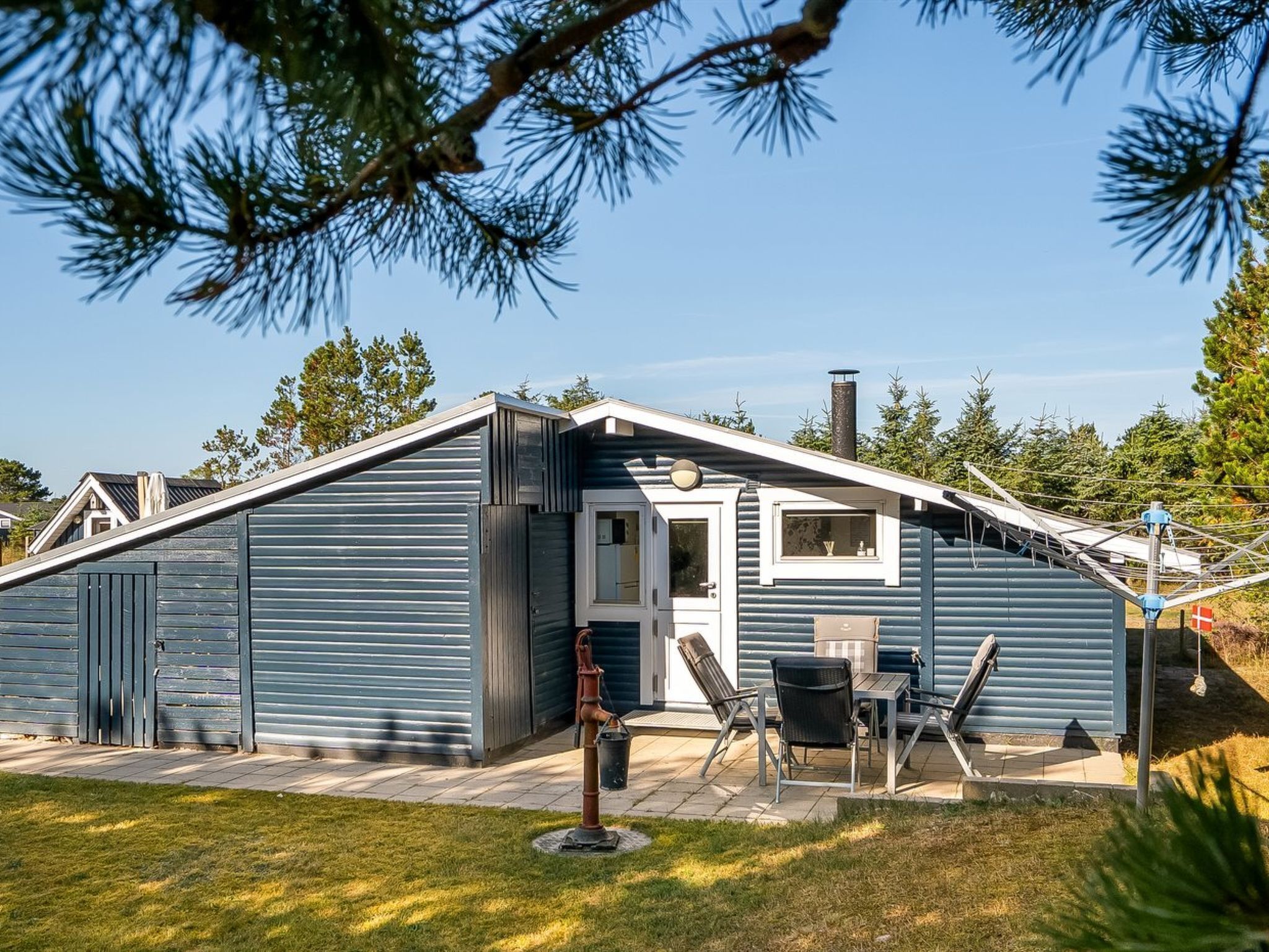 Une cabane de plain-pied avec un toit à pignon, une porte d’entrée et un petit patio comprenant une table et des chaises.