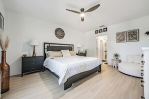 A bedroom with a bed, bedside tables, a ceiling fan, a wall-mounted decorative item, and a door leading to another room. - 5 BR Home/Sleeps 10/3 Offices/Fenced/Garage (Zephyrhills)
