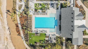 Vista aérea de un resort con una piscina grande, zonas de descanso y una playa.