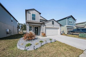 A residential house with a garage, a driveway, and a landscaped front yard with a small bush and gravel. - 5 BR Home/Sleeps 10/3 Offices/Fenced/Garage (Zephyrhills)
