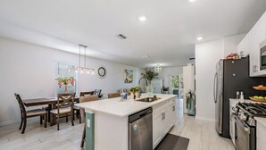Una cocina moderna con una isla central, electrodomésticos integrados y un comedor con sillas de madera.