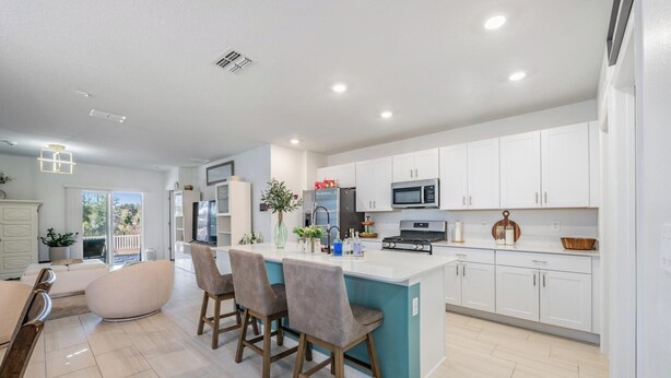 Una cocina moderna con armarios blancos, una isla central con taburetes y un comedor con mesa y sillas blancas.