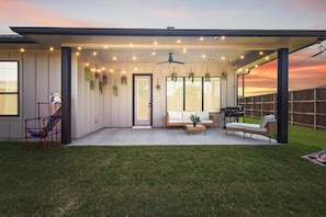 Eine überdachte Terrasse mit Lichterketten, einem Deckenventilator und einer Sitzecke mit Sofa und Tisch.