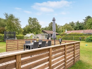 A wooden deck with a table and chairs, surrounded by a fence, with a house and greenery in the background. - "Melisande" -  from the sea by Interhome (Storvorde)