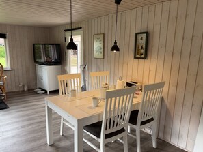 A dining area with a wooden table and chairs, a television, and a clock on the wall. - "Melisande" -  from the sea by Interhome (Storvorde)