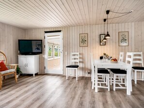 A room with a television on a cabinet, a dining table with chairs, and a door leading outside. - "Melisande" -  from the sea by Interhome (Storvorde)