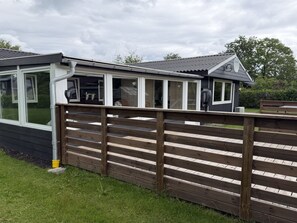 A wooden deck with a view of a house with large windows and a covered porch. - "Melisande" -  from the sea by Interhome (Storvorde)