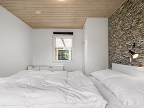 Une chambre avec deux lits, une fenêtre, un mur en pierre et un luminaire au plafond.