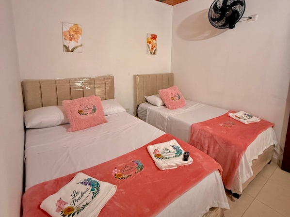 Two single beds with headboards, pink towels, and a fan on the wall.
