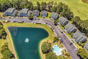 Ein Golfplatz mit Teich, Schwimmbecken und einer Reihe moderner Gebäude mit Parkplätzen.