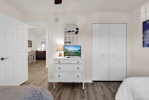 Ein Schlafzimmer mit Fernseher auf einer Kommode, einem Kleiderschrank und einer Tür zu einem weiteren Raum.