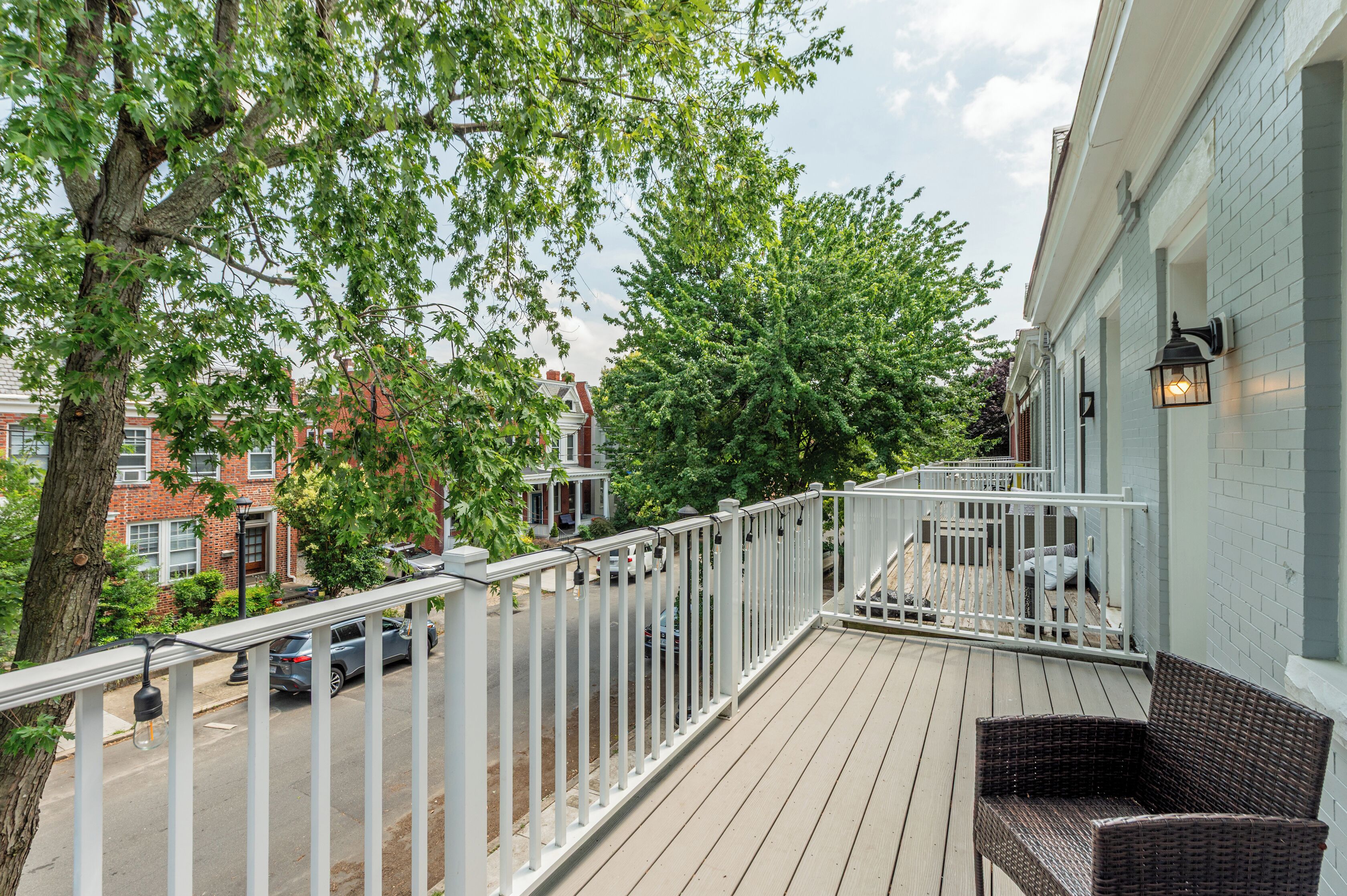 Un balcon doté d'une balustrade blanche, de meubles en osier et offrant une vue sur une rue bordée de voitures garées et d'immeubles.