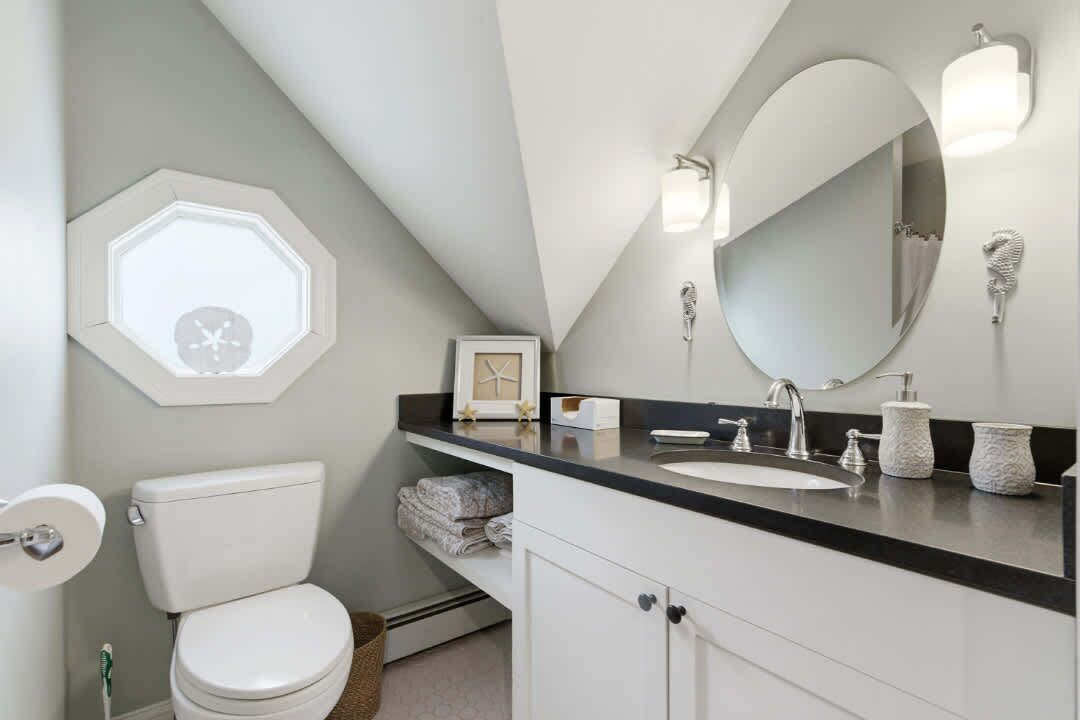 A bathroom with a white toilet, a black countertop, a large mirror, and a hexagonal light fixture.