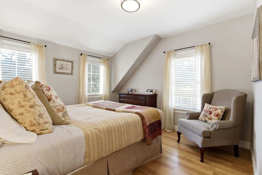 A bedroom with a bed, a chair, a dresser, and a picture on the wall.