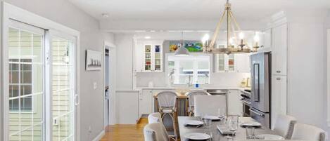 A modern kitchen with white cabinets, a dining area with a wooden table and chairs, and a chandelier.