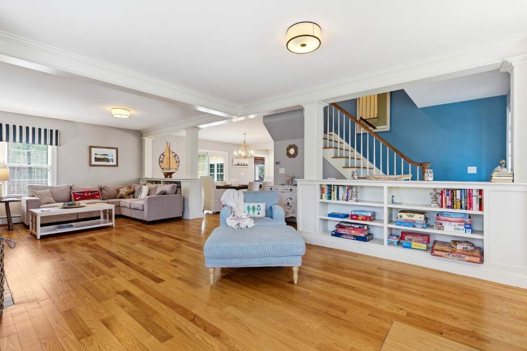 A spacious living room with a wooden floor, a blue sofa, a white coffee table, a bookshelf, and a staircase with blue walls.