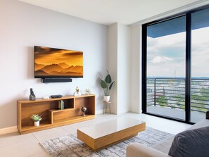 Ein modernes Wohnzimmer mit großem Fernseher, einer Holz-Unterhaltungseinrichtung und Blick auf eine Skyline durch ein großes Fenster.