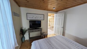 Een slaapkamer met een bed, een televisie op een dressoir, een deur naar een balkon en een muur met een inspirerende quote.