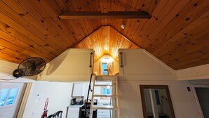 Een kamer in loftstijl met een schuine plafond, een ventilator, een ladder en een keukenhoek.