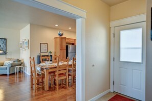 Una sala de estar con sofá, una mesa de comedor con sillas, armarios de madera, un refrigerador y una puerta con ventana.