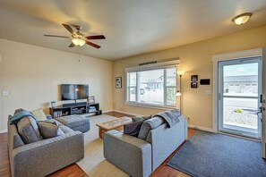 A living room with a ceiling fan, a flat-screen TV, and a large window with blinds.
