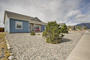 A residential house with a gravel driveway, a small front yard with a tree, and a clear sky.