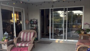 En overdækket terrasse med fletningsmøbler, en loftsvifte og udsigt til omgivelserne gennem glasdøre.