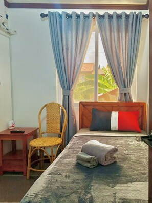 Una camera d'albergo con un letto, una sedia, un tavolino e una finestra con tende.