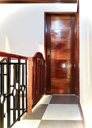 Eine Holztür mit einem Metallgitter, einem Schachbrettfußboden und einem Lichtschalter an der Wand.