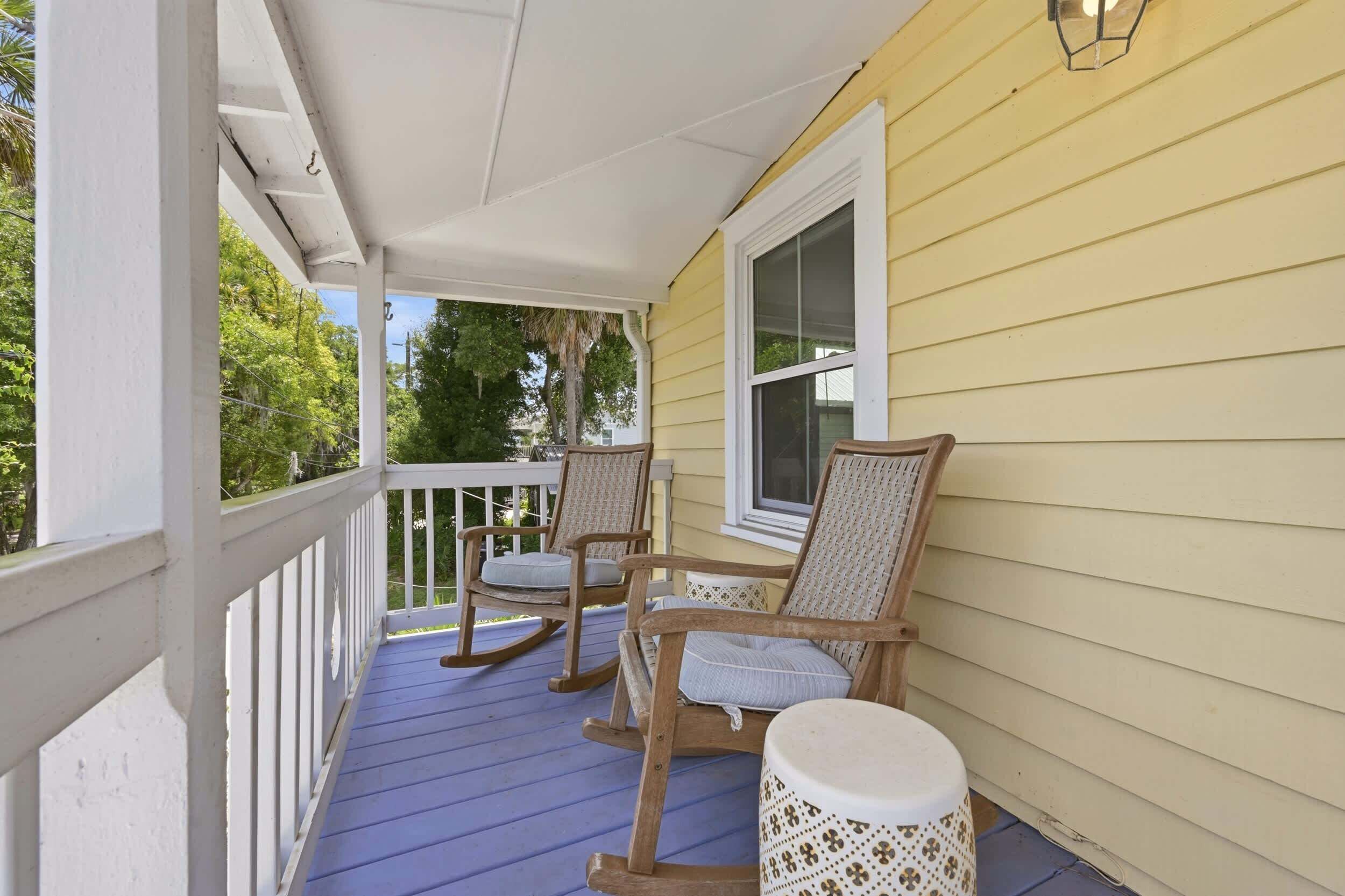 A porch with two rocking chairs and a small table, overlooking a green landscape.