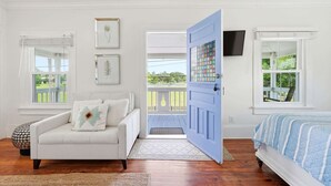 A room with a white sofa, a bed with a blue and white striped bedspread, a blue door, and a balcony with a white railing. - Porch on Pine Downtown (St. Augustine)