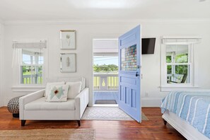 Ein Zimmer mit einem weißen Sofa, einem Bett mit einer blau-weiß gestreiften Tagesdecke, einer blauen Tür und einem Balkon mit einer weißen Brüstung.