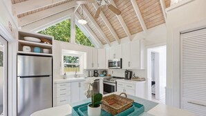 A kitchen with white cabinets, stainless steel appliances, and a teal tray with a potted plant. - Porch on Pine Downtown (St. Augustine)