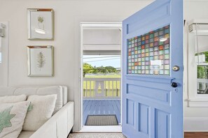 Ein Zimmer mit einem weißen Sofa, einer blauen Tür mit Glasmalerei und Blick auf einen Balkon mit Geländer.