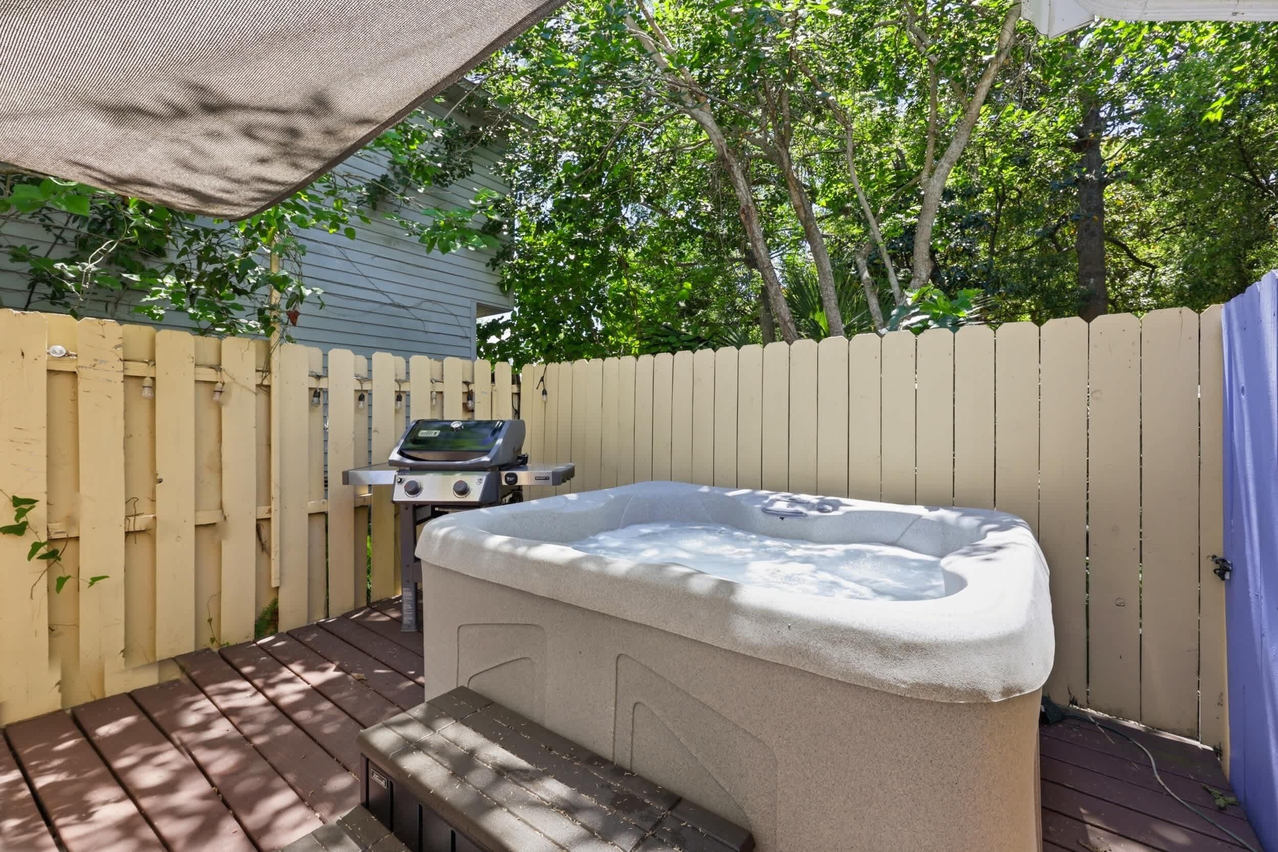 A hot tub on a wooden deck with a fence and trees in the background.