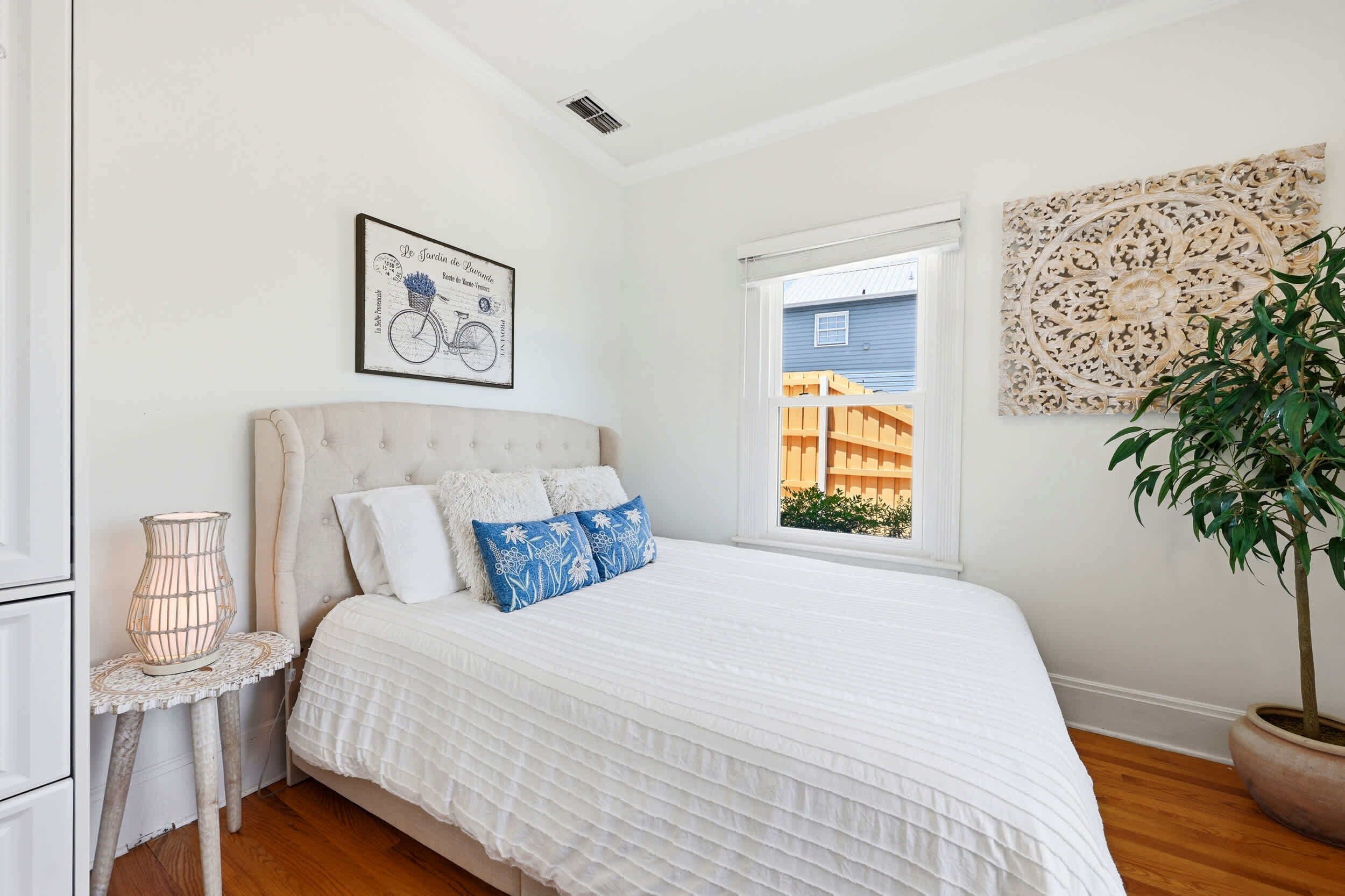 A bedroom with a bed, a window, a wall decoration, and a potted plant.
