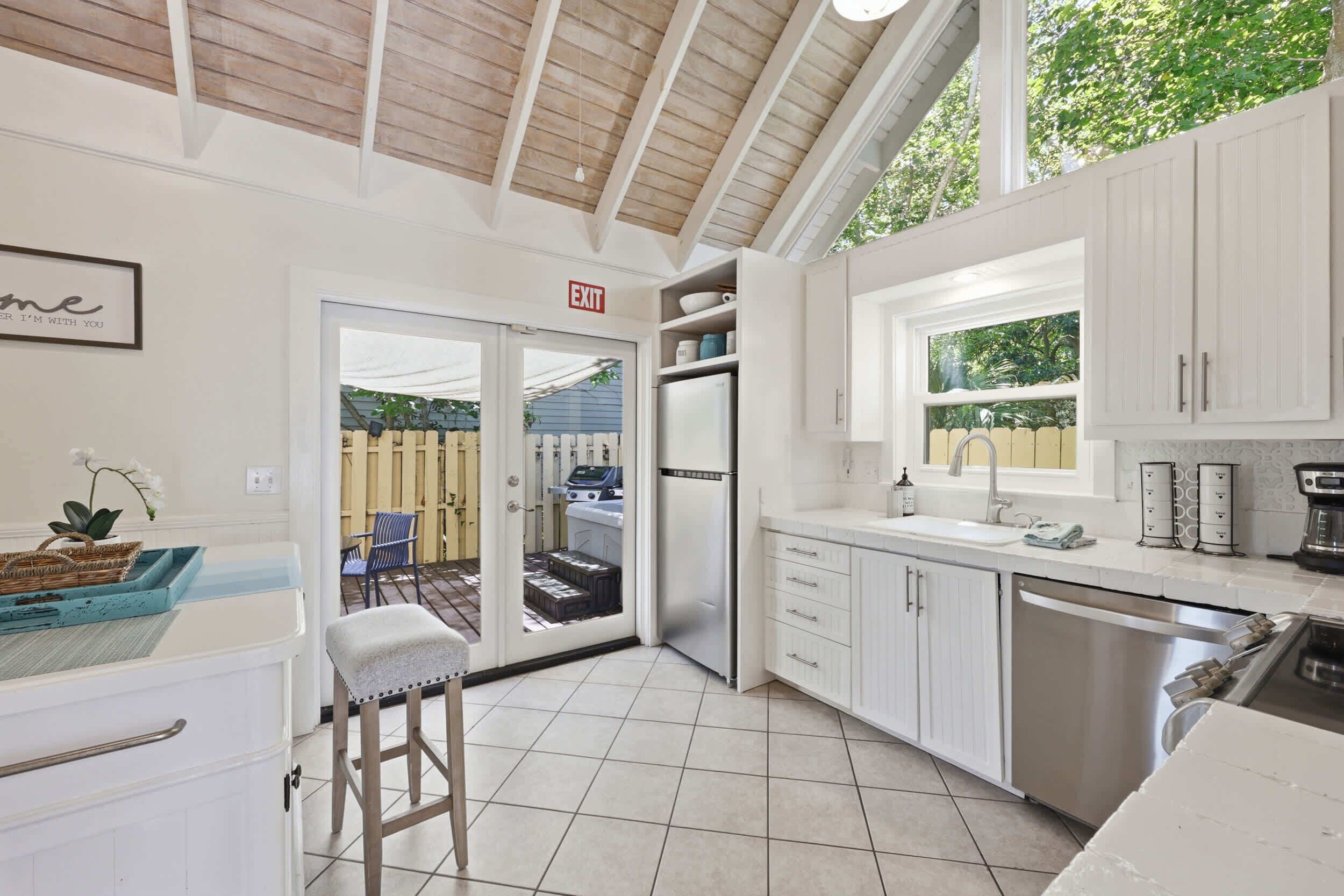 A modern kitchen with white cabinetry, a stainless steel refrigerator, a built-in oven, and a window overlooking a backyard.