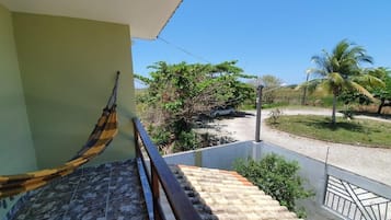 A staircase with a hammock, leading to a balcony overlooking a garden with palm trees.