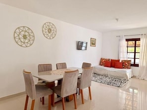 Un comedor con una mesa y sillas, una cama con almohadas y un televisor en la pared.