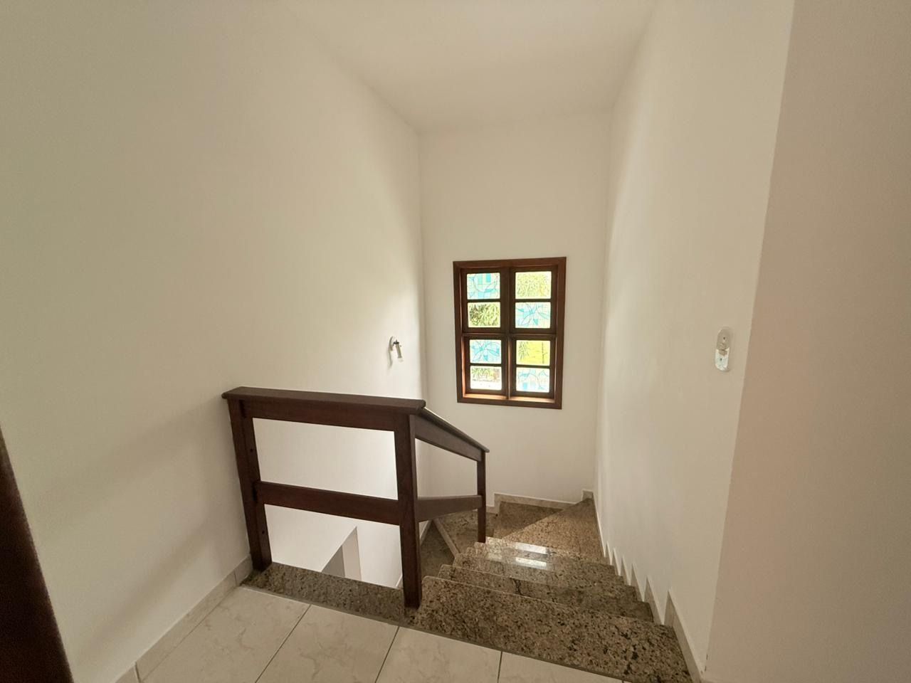 A narrow stairway with a wooden handrail, a small window with a view, and a light switch on the wall.