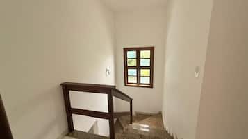 A narrow stairway with a wooden handrail, a small window with a view, and a light switch on the wall.