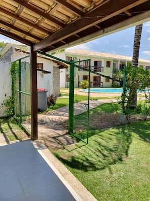 Un patio techado con piscina, un jardín cercado y un edificio al fondo.