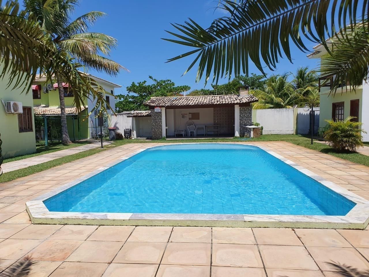 Una piscina rectangular con una solana con mosaicos, rodeada de palmeras y un edificio con techo de tejas.