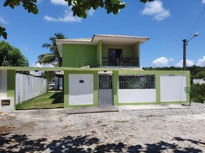 Una casa de dos pisos con fachada verde y blanca, un balcón y un acceso con portón.