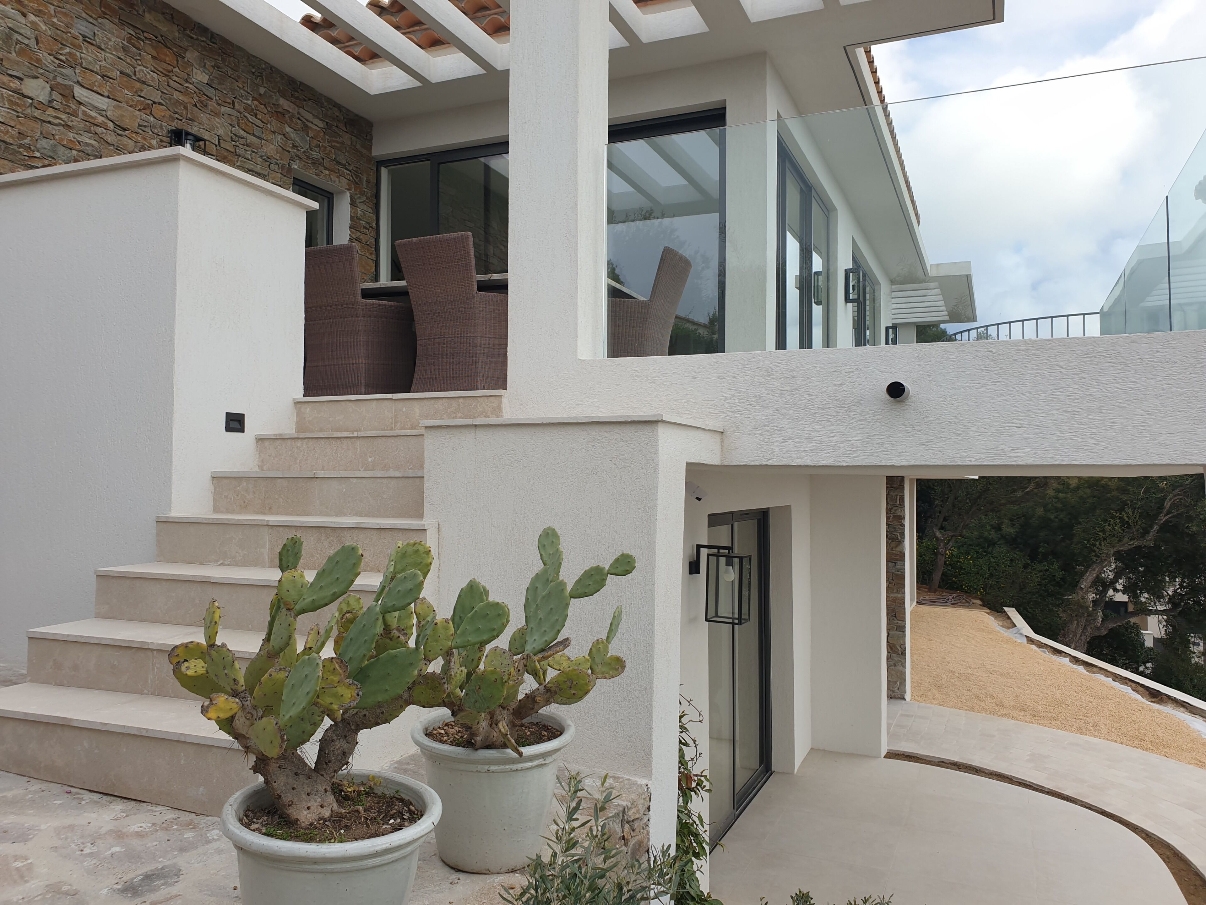 Una casa moderna amb façana de pedra, una porta de vidre i una escala que condueix a un balcó.