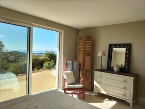 A bedroom with a large sliding glass door leading to a balcony, a chair, a dresser, and a mirror. - A CONTEMPORARY VILLA WITH AN EXCEPTIONAL PANORAMA (La Croix-Valmer)