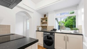 A modern kitchen with a built-in washing machine, white cabinetry, and a window with a view of greenery. - Elegant 3 bedroom | 2 Bath | In Burnley (Lancashire)