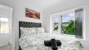 A bedroom with a bed, a window with a view, a painting on the wall, and a door. - Elegant 3 bedroom | 2 Bath | In Burnley (Lancashire)